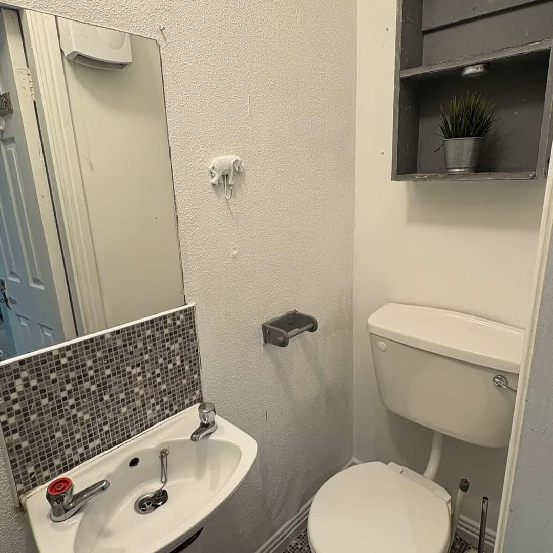 Small bathroom with toilet, sink, mirror, mosaic tile backsplash, and wall decor.
