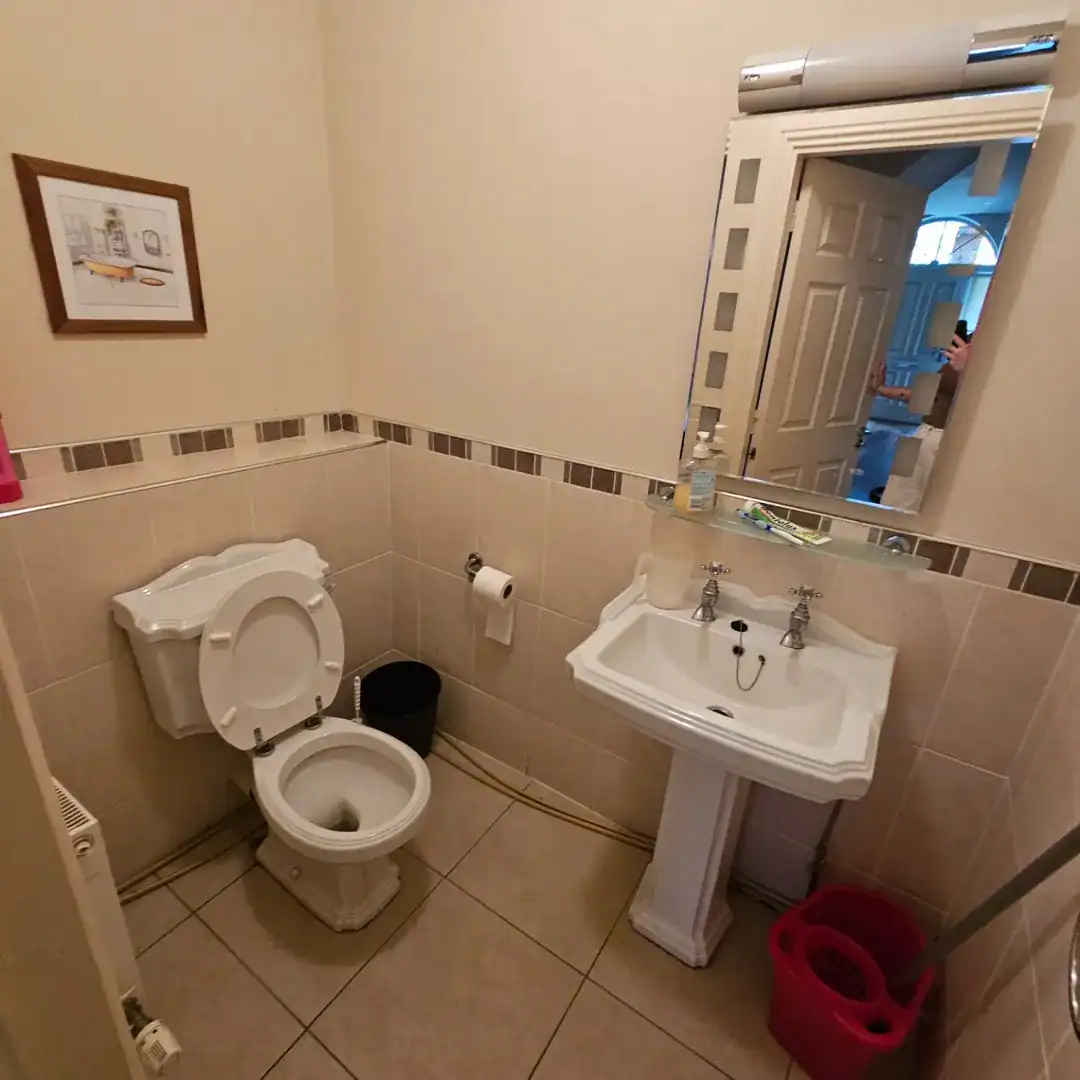 Small bathroom with toilet, sink, mirror, and tiled walls.