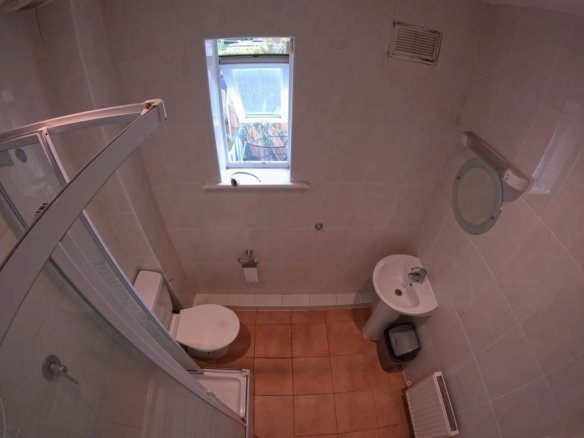 Compact bathroom with toilet, sink, shower, and small window.