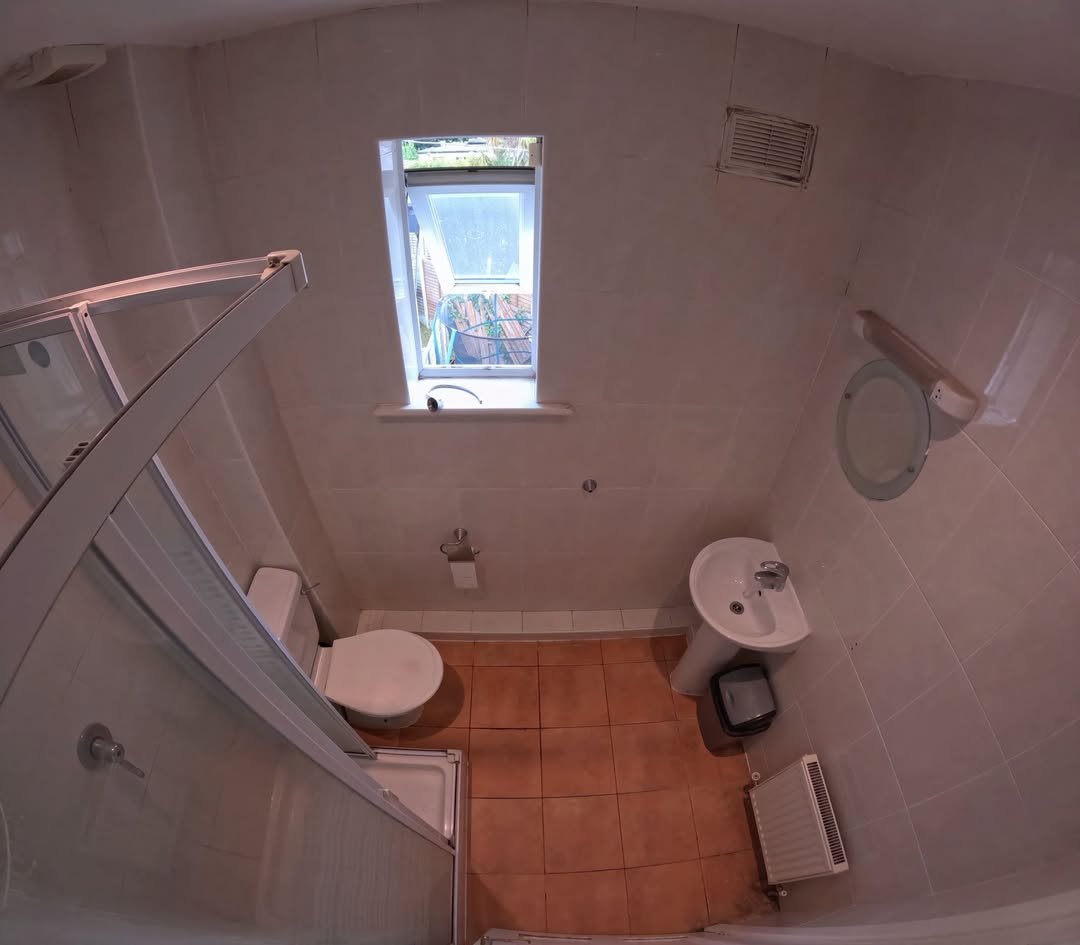 Compact bathroom with toilet, sink, shower, and small window.