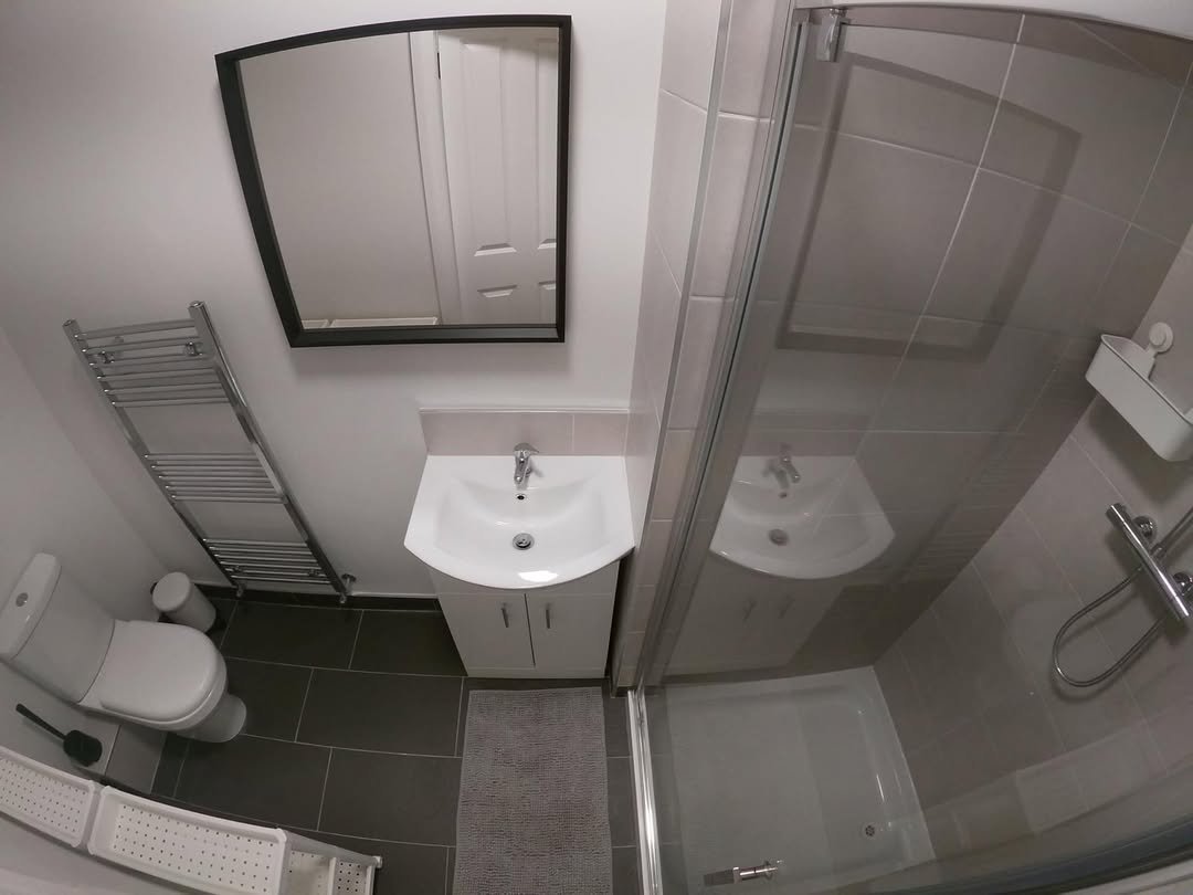 Small bathroom with toilet, sink, heated towel rack, mirror, and shower.