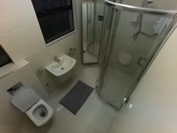 Small bathroom with toilet, sink, shower, and mirror cabinet. Neutral tones.