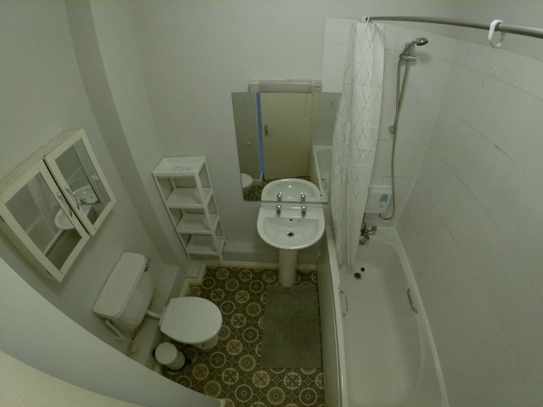 Compact bathroom with toilet, sink, shower-tub combo, and storage shelf.