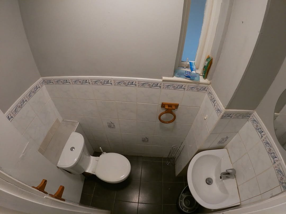 Small bathroom with toilet, sink, and blue accents. Tiled walls and floor. Overhead view.