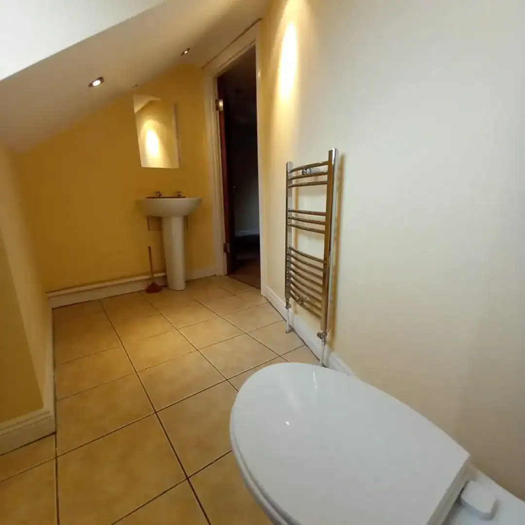 Small bathroom with toilet, sink, heated towel rack, and yellow walls.