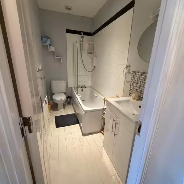 Small bathroom with tub, toilet, sink, and gray/white decor.