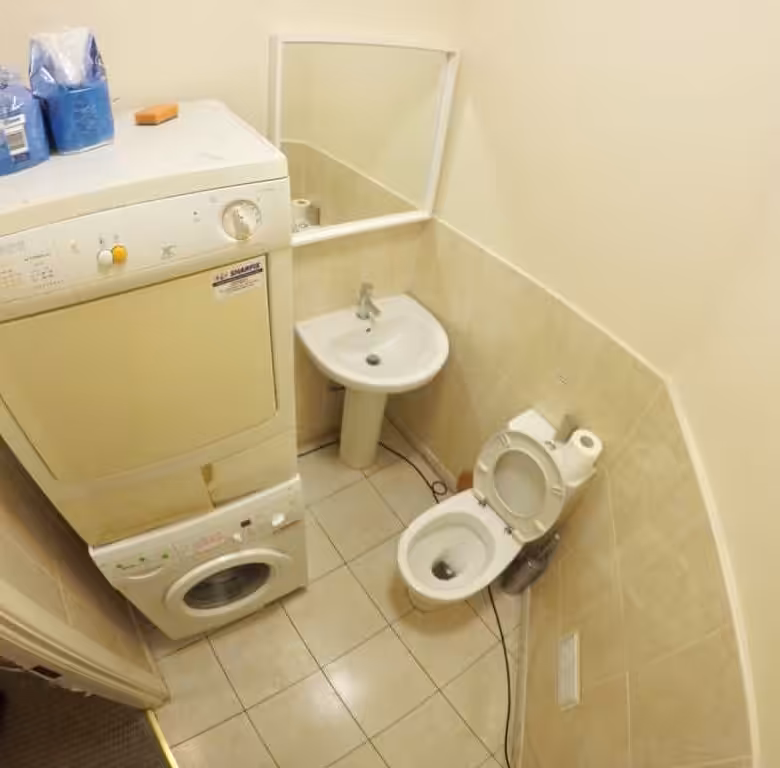 Small bathroom with stacked washer and dryer, toilet, and sink with mirror.
