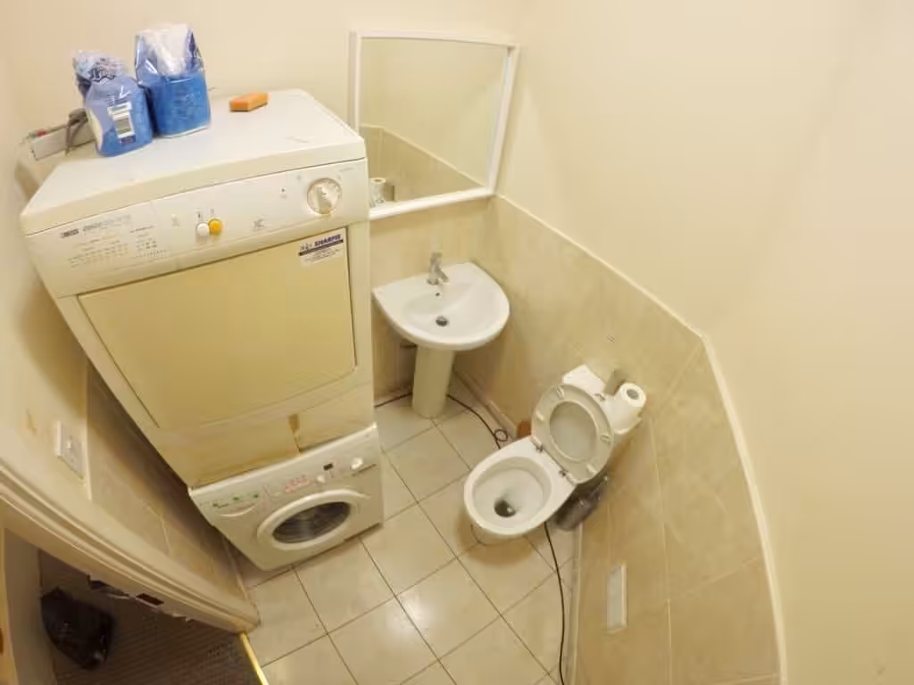 Small bathroom with stacked washer and dryer, toilet, and sink with mirror.