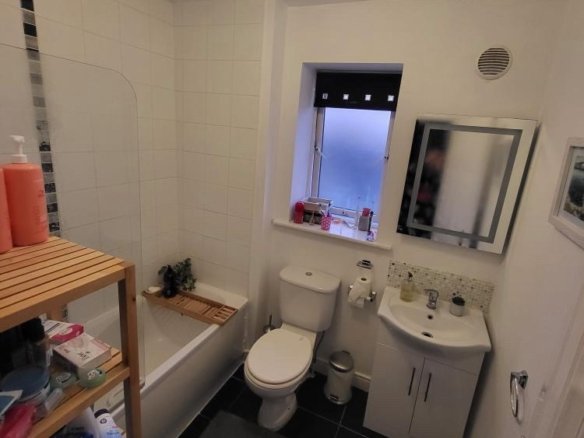 Small bathroom with white tiles, black floor, toilet, sink, and shower.