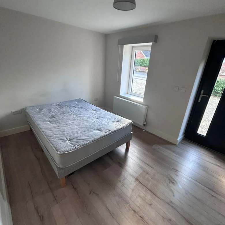 Small bedroom with bed, window, and light wood floors.