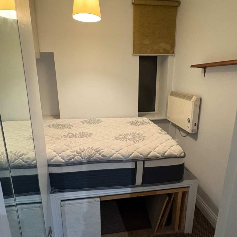 Small bedroom with raised bed, window, and wall heater.