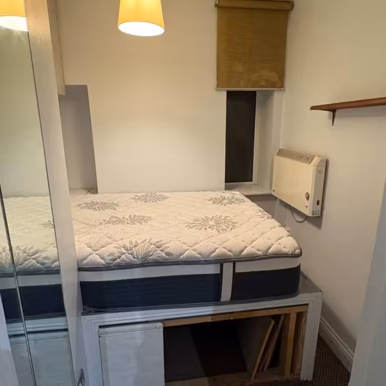 Small bedroom with raised bed, storage underneath, and window.