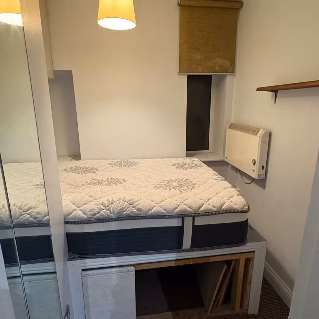 Small bedroom with raised bed, storage underneath, and window.