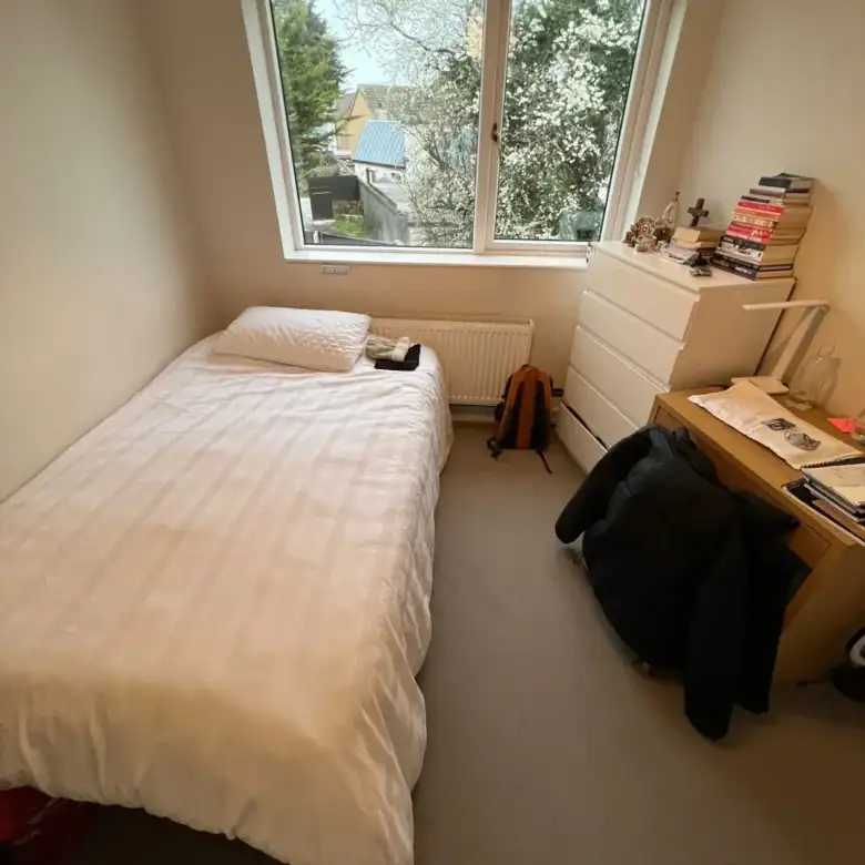 Small bedroom with single bed, dresser, desk, and window view.