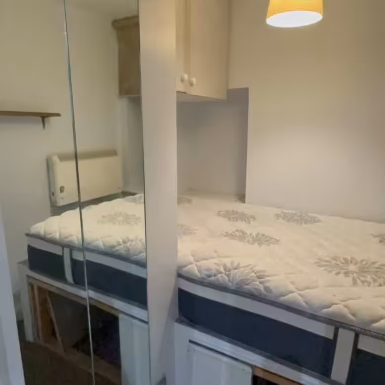 Cozy bedroom with bed, storage cabinets, and a mirrored wall. Simple interior design.