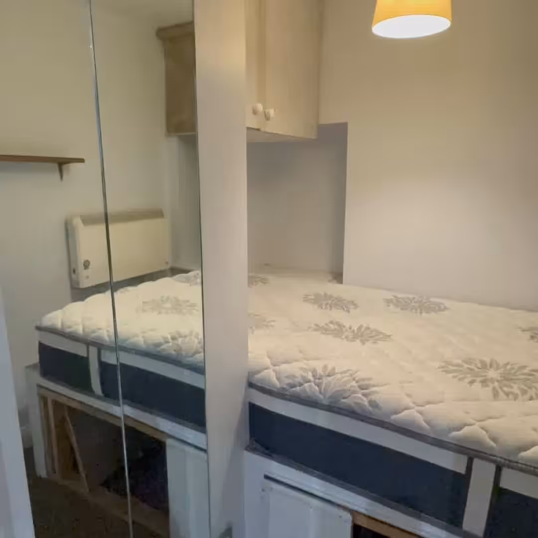 Cozy bedroom with bed, storage cabinets, and a mirrored wall. Simple interior design.