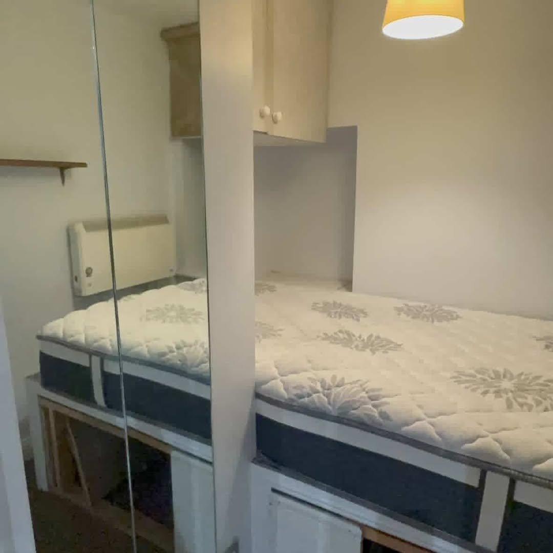 Cozy bedroom with bed, storage cabinets, and a mirrored wall. Simple interior design.