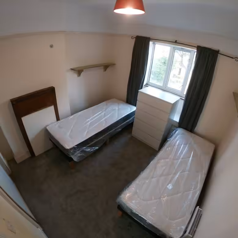 Small bedroom with two twin beds, dresser, shelves, and window with curtains. Compact living space.