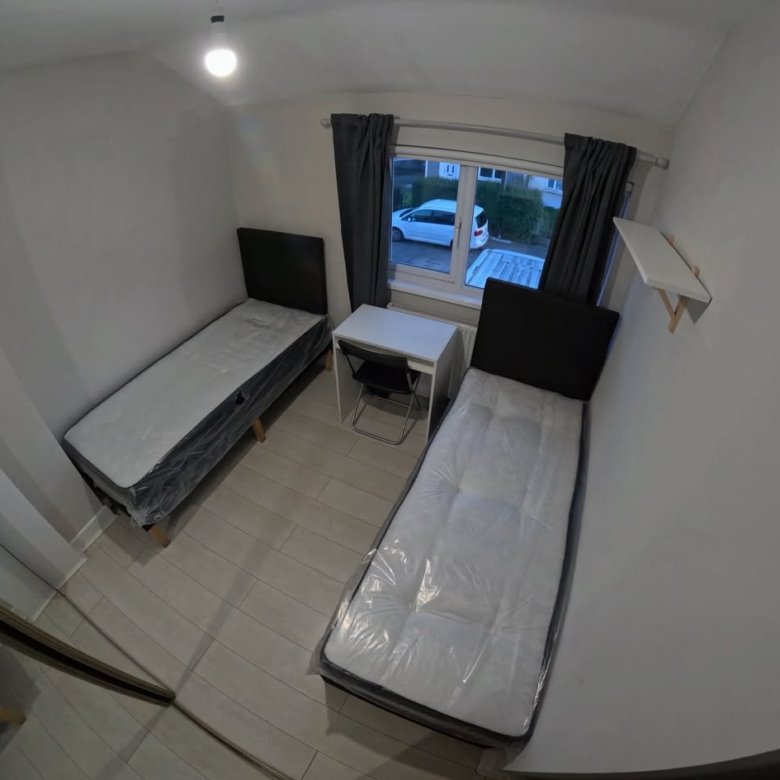 Small bedroom with two single beds, desk, and window with natural light.