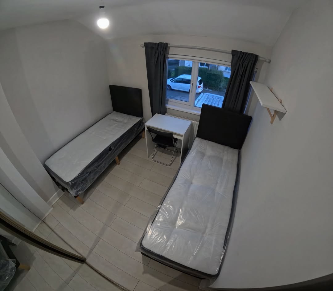 Small bedroom with two single beds, desk, and window with natural light.