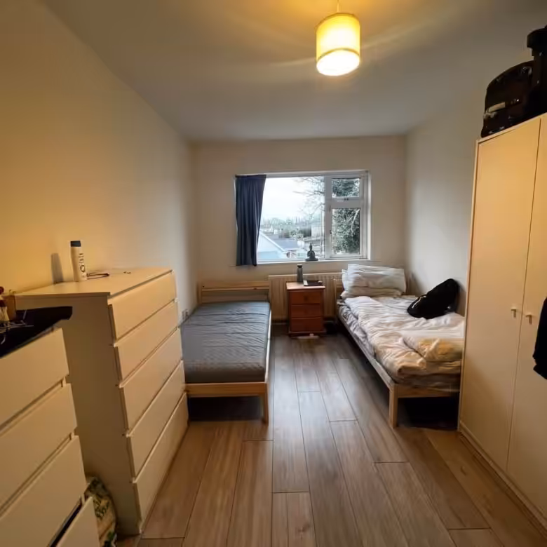 Small bedroom with two single beds, dresser, and wardrobe near a window.