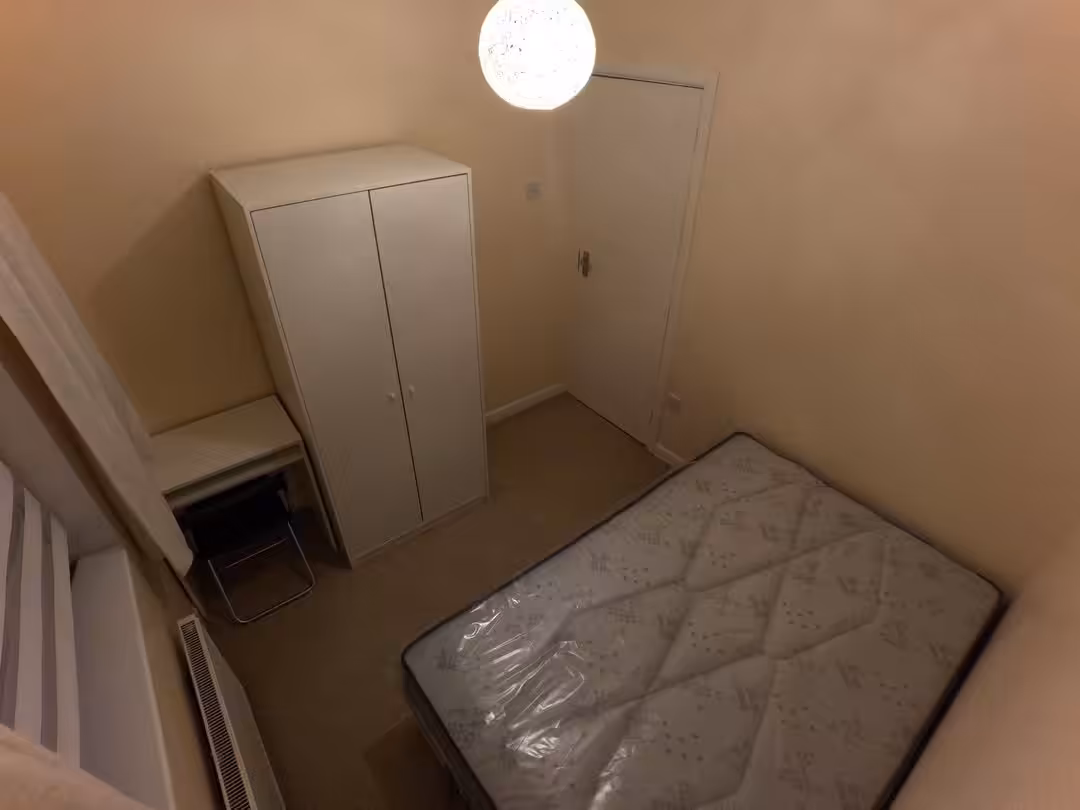 Bedroom with bed, wardrobe, desk, and radiator in a small, cozy space. Neutral colors.