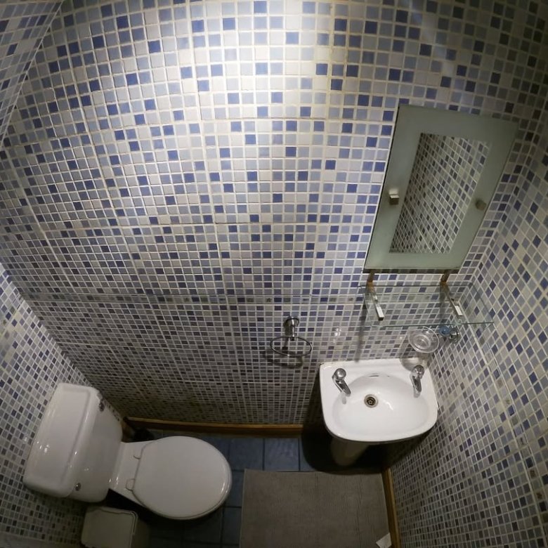 Small bathroom with blue tile, toilet, sink, and mirror.