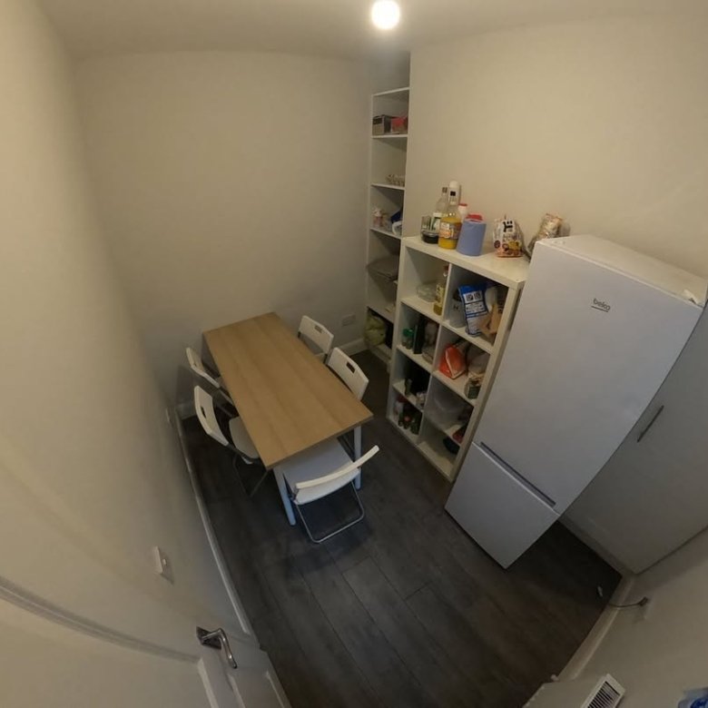Small dining area with table, chairs, shelves, and refrigerator.
