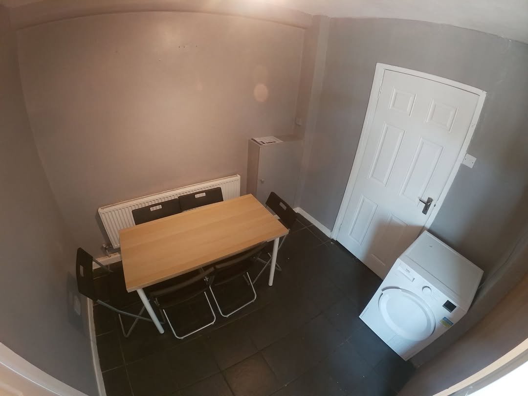 Small dining area with table, chairs, washing machine, and radiator in a compact room with gray walls.