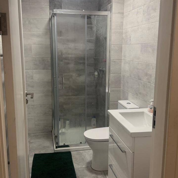Small bathroom with shower, toilet, and vanity. Gray tile walls and floor.