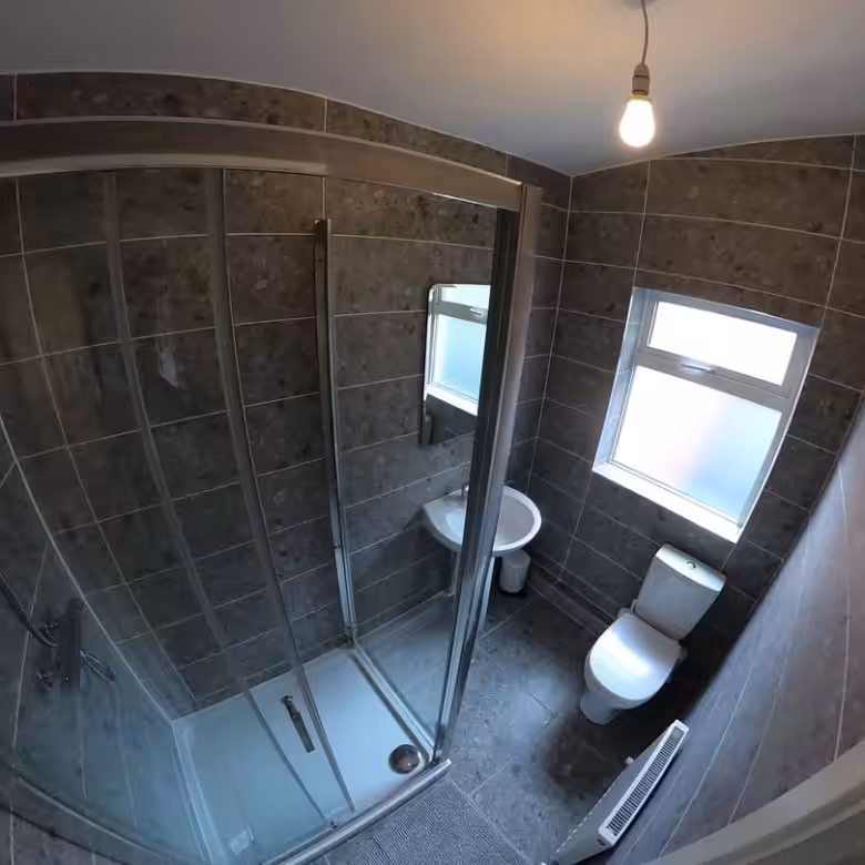 Small bathroom with gray tile, shower, toilet, and sink. Modern design.