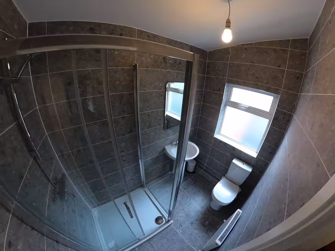 Small bathroom with gray tile, shower, toilet, and sink. Modern design.