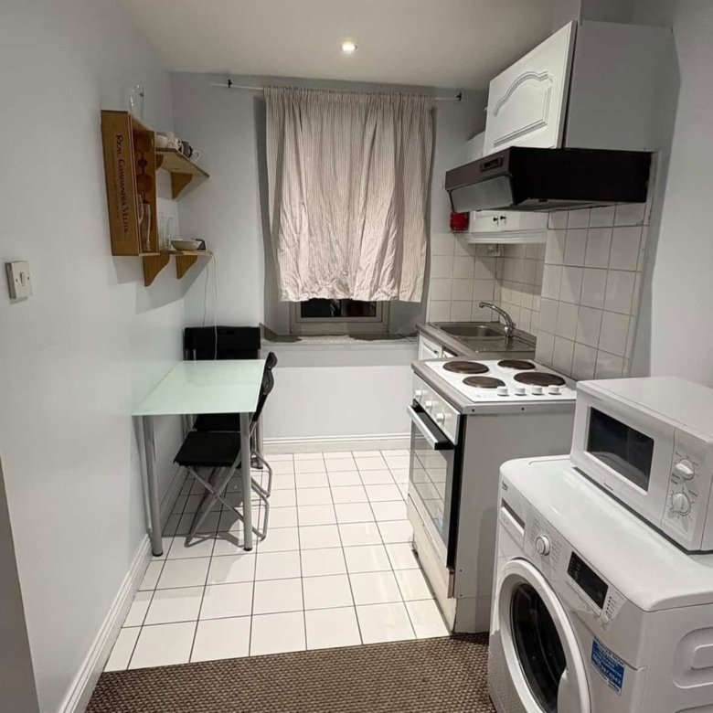 Small kitchen with appliances, table, and window. White tile floor and walls.