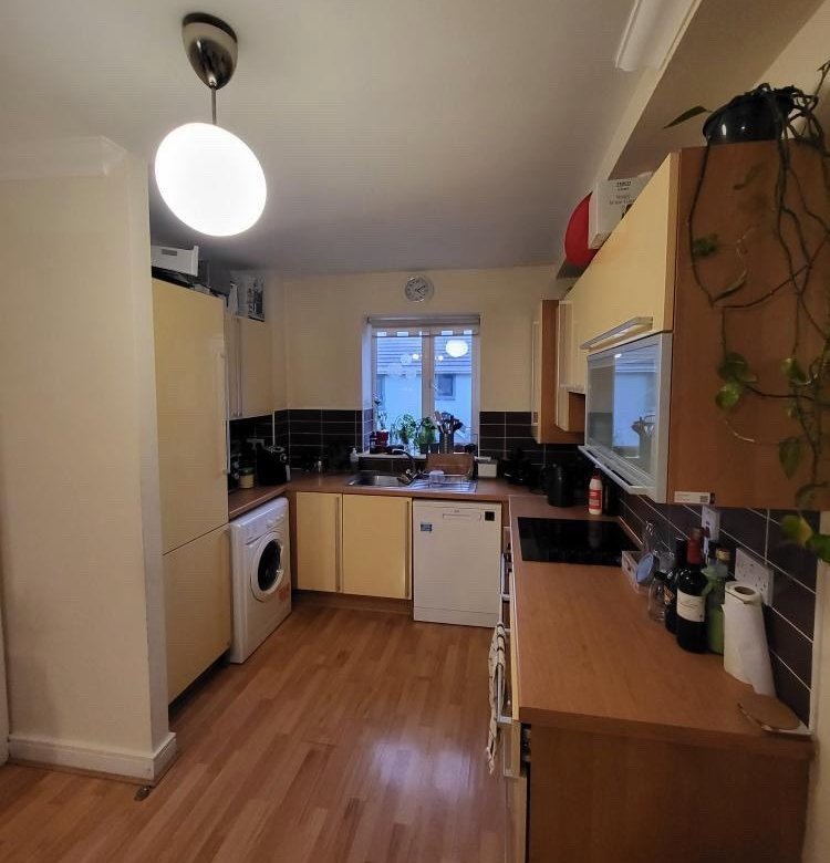 Compact kitchen with light wood cabinets, appliances, and a window.