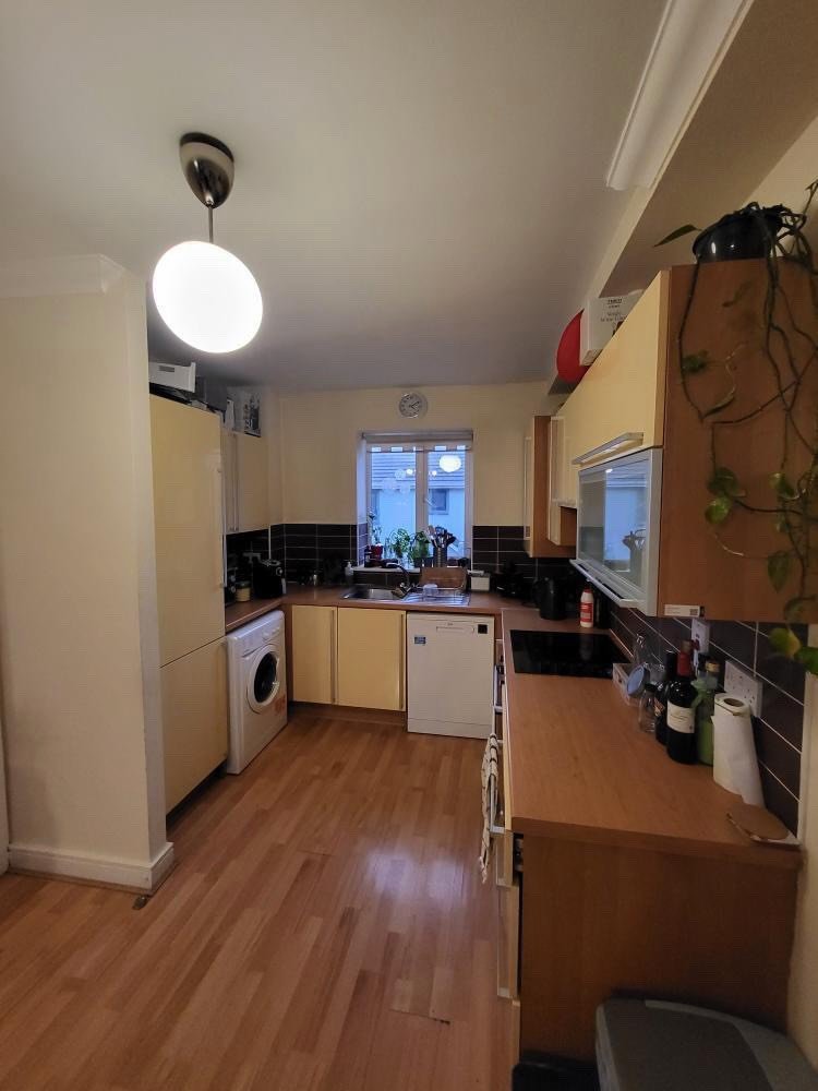 Compact kitchen with light wood cabinets, appliances, and a window.