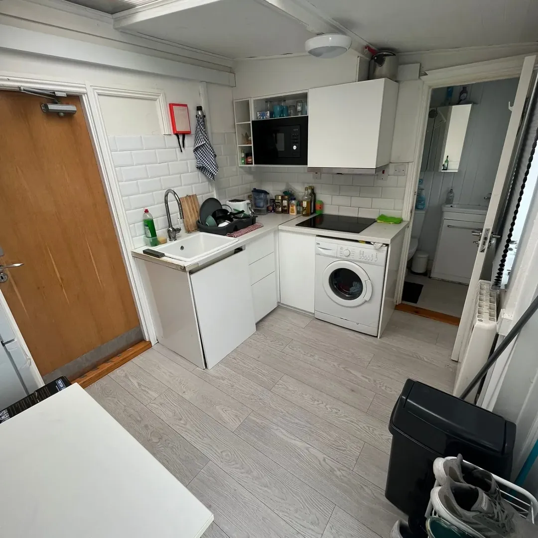 Small kitchen with washing machine, sink, microwave, and white cabinets in a compact space.