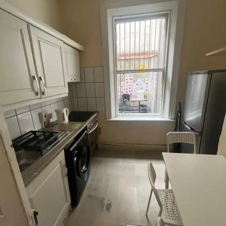 Small kitchen with white cabinets, appliances, table, and a window overlooking a courtyard.