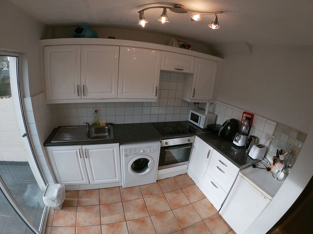 Small kitchen with white cabinets, gray countertops, and terracotta tile flooring.