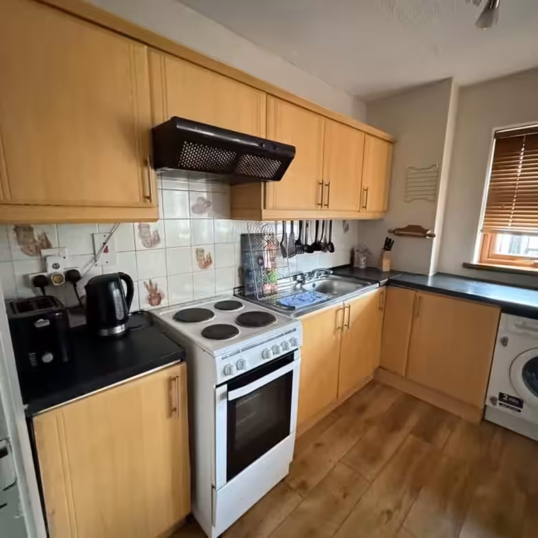 Compact kitchen with light wood cabinets, white stove, and dark countertops.