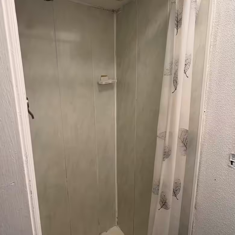 Small shower stall with marble-effect panels and a leaf-patterned shower curtain.