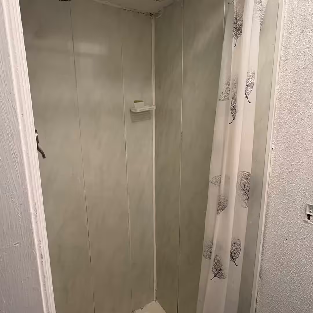Small shower stall with marble-effect panels and a leaf-patterned shower curtain.