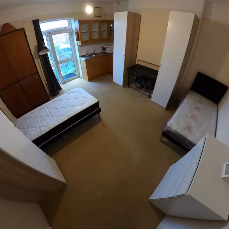 Small studio apartment with two beds, kitchenette, wardrobe, and desk. Compact living space.