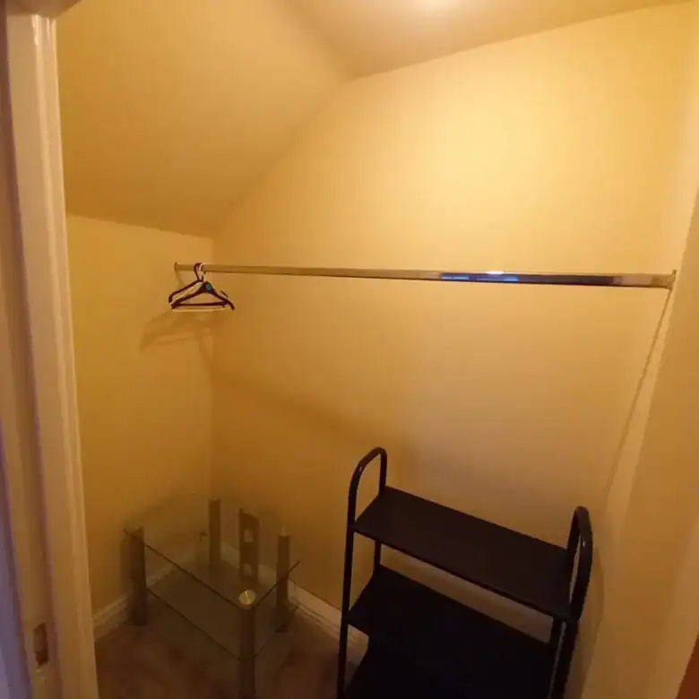Small walk-in closet with hanging rod, glass table, and black shelving unit.