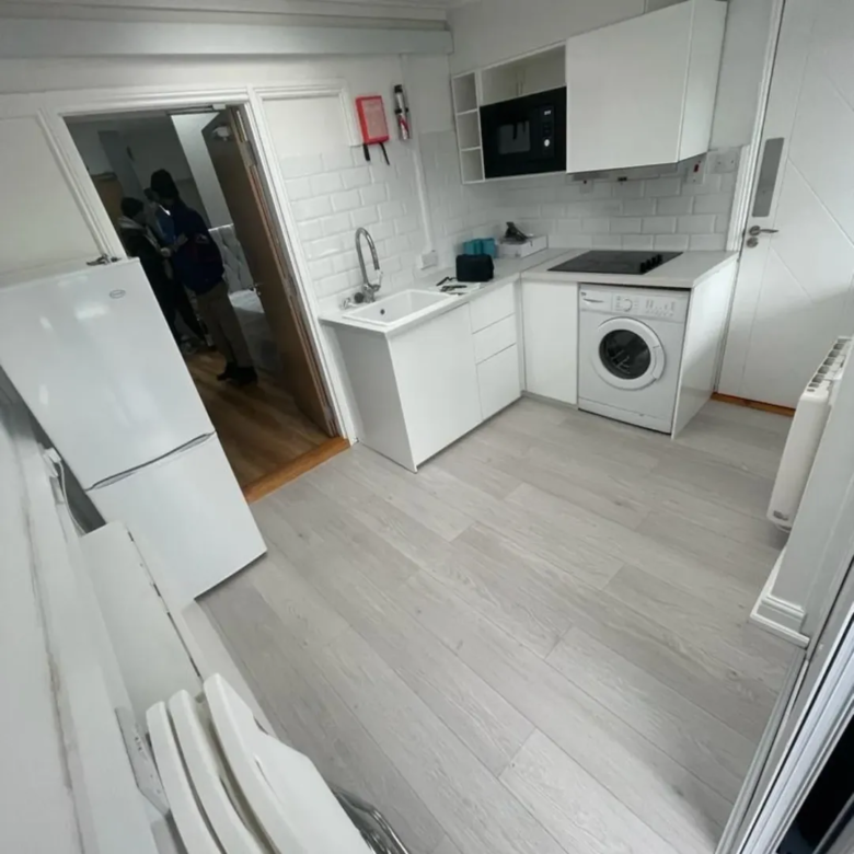 Small white kitchen with fridge, sink, washing machine, and cabinets.