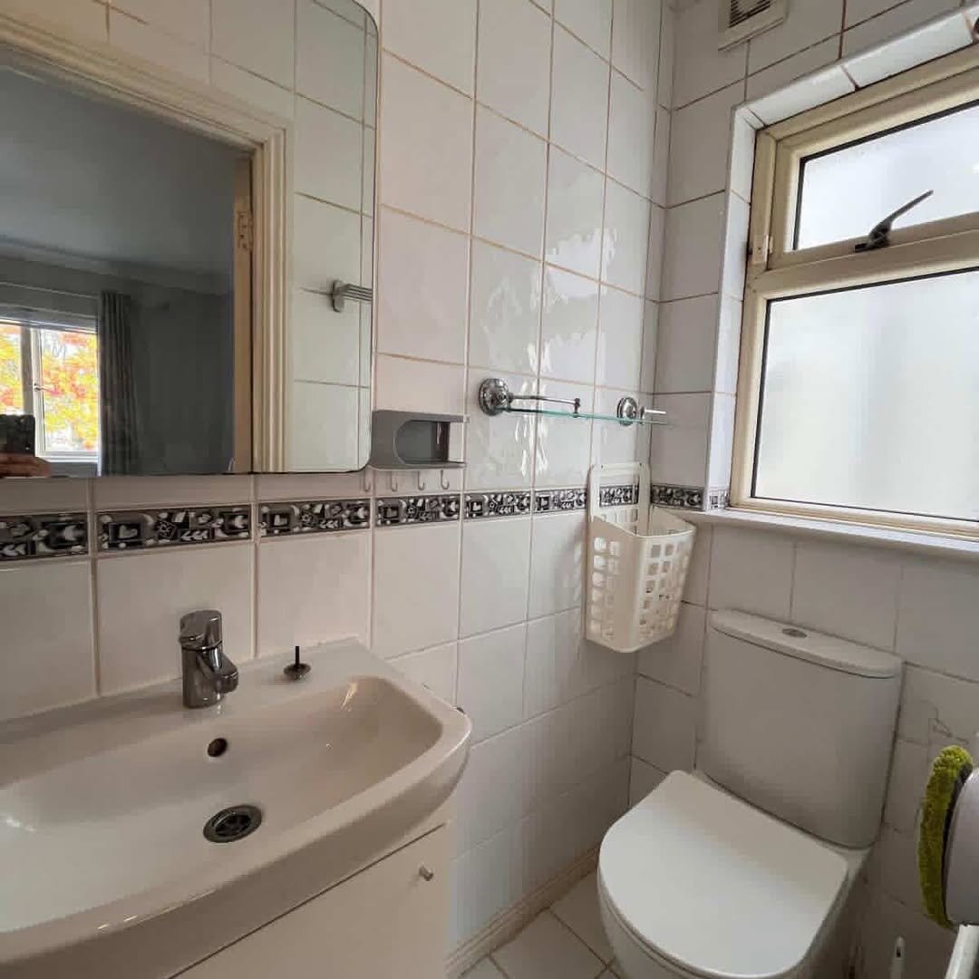 Small bathroom with white tiles, sink, and toilet near a window.