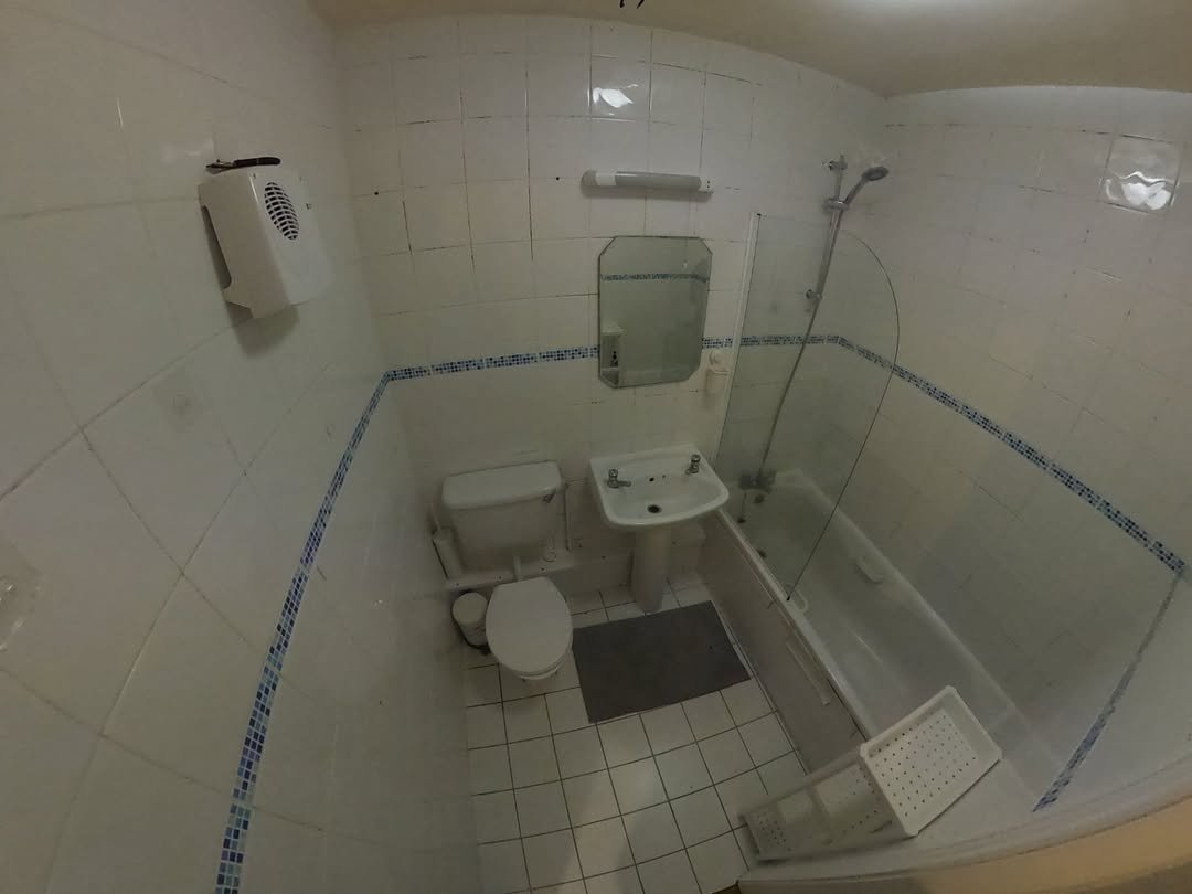 Small bathroom with white tiles, toilet, sink, and bathtub with glass screen.
