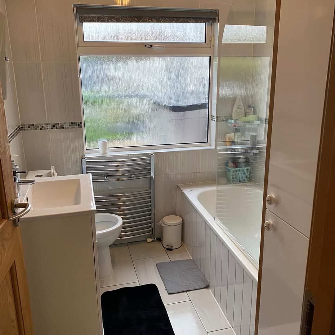 Small bathroom with white tiles, tub, sink, and heated towel rack.