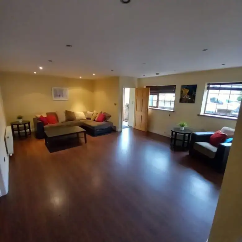 Spacious living room with dark wood floors, brown sectional sofa, and natural light from windows.