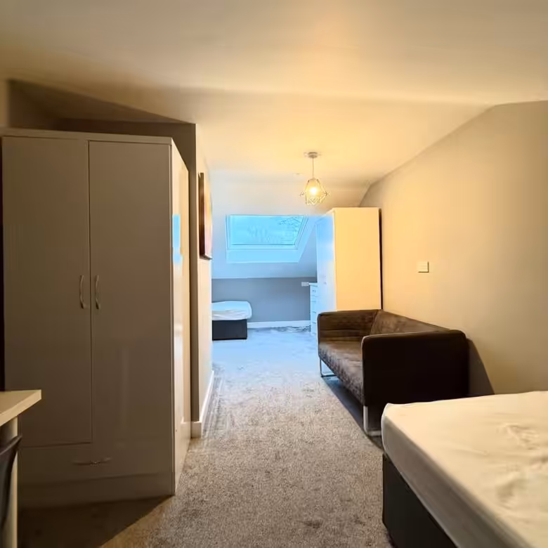 Bright studio apartment interior with a sofa, bed, wardrobe, and skylight. Neutral color scheme.