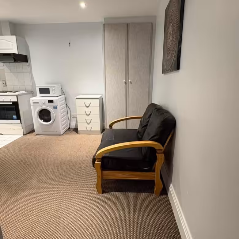 Studio apartment with washing machine, microwave, small sofa, drawers, and wardrobe. Neutral color scheme.